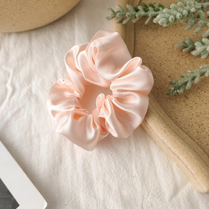 Close-up of soft pink satin scrunchie with silky luster on a minimal white background