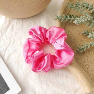 Detail of a bright rose pink satin scrunchie with silky folds on a white textured table