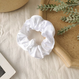 Detail of white satin scrunchie showing glossy fabric texture and pleated design
