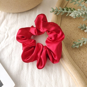 Detailed view of red satin scrunchie with soft silk luster and natural pleats texture