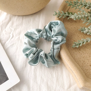 Detail of light blue satin scrunchie showing smooth texture and elegant folds on fabric