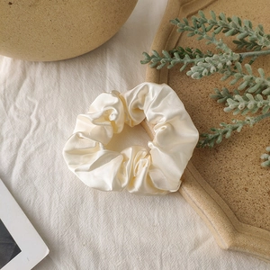 Detail of a creamy satin scrunchie with soft folds and elegant pearl luster finish