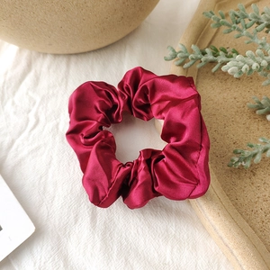 Close-up of a burgundy satin scrunchie with a soft silk texture on a cozy background