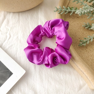 Detail of glossy purple satin scrunchie showing soft texture and elastic design