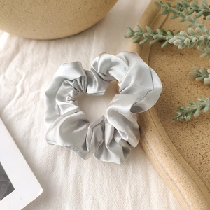 Detailed view of silver satin scrunchie with silky texture and elegant shine on linen