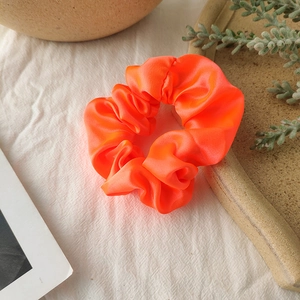 Close-up of a vibrant neon orange satin scrunchie on white textured fabric background