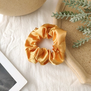 Macro view of a vibrant yellow satin scrunchie with elegant folds on textured linen fabric