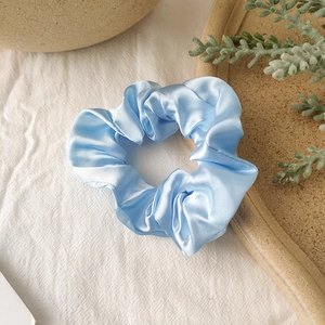 Close-up of light blue satin scrunchie with silky folds and premium fabric texture
