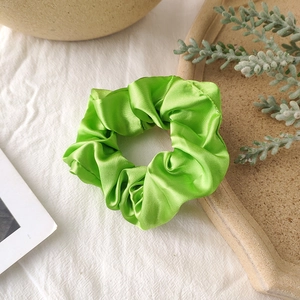 Detail of vibrant green satin scrunchie with silk gloss on a minimalist background