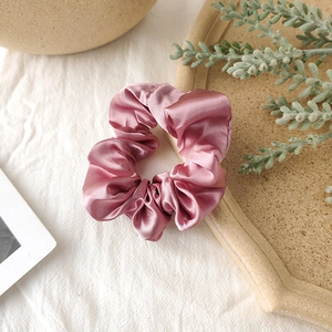 Detailed view of pink satin scrunchie showing glossy fabric texture on linen background