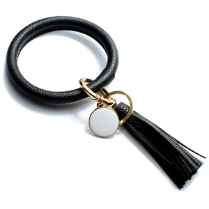 Detail of black leather ring keychain with gold clasp, tassel, and white enamel charm