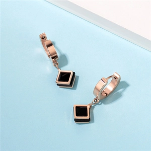 Minimalist rose gold hoop earrings with black geometric square charm on a light blue background