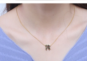 Detail shot of a gold puzzle piece necklace worn by a woman with a purple sweater
