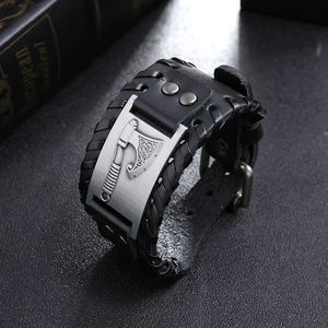 Detail of a vintage black wide leather bracelet with a metal Viking axe charm and braided texture