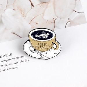 Enamel pin featuring a miniature astronaut inside a coffee cup with I Need My Space text