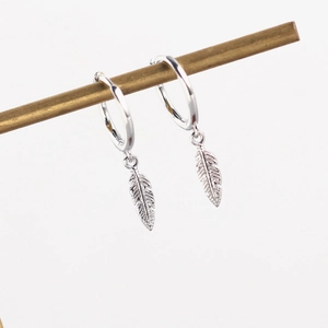 Macro detail of silver feather pendants hanging from elegant hoop earrings for women