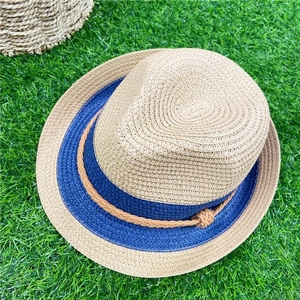 Detail of light beige straw panama hat with navy ribbon and brown cord on green grass