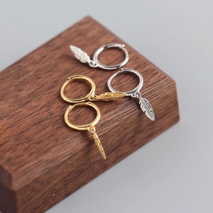 Close-up of gold and silver feather charm hoop earrings on a wooden stand