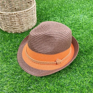 Brown woven straw fedora hat with orange decorative band on a green lawn background