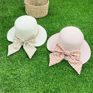 Detail of straw sun hats with large plaid bows in cream and pink on a green lawn
