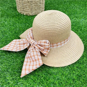 Women's straw sun hat with orange checkered ribbon bow on green grass background