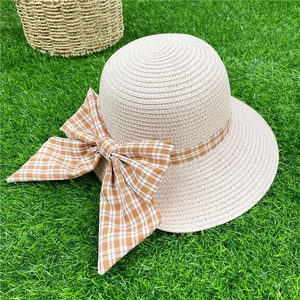 Beige straw sun hat with orange gingham bow on green lawn for summer beach vacation