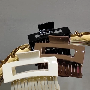 Three large rectangular hair claws in black, coffee, and beige on a vintage mirror