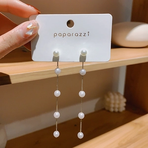 Detailed view of long gold tassel earrings with elegant white pearls on display card