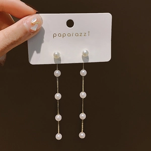 Detailed view of long gold tassel earrings with white pearls on a branded display card