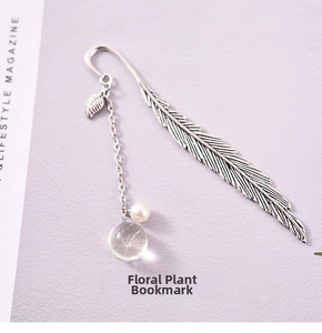 Detail of silver feather bookmark with dandelion glass bead and pearl on purple surface