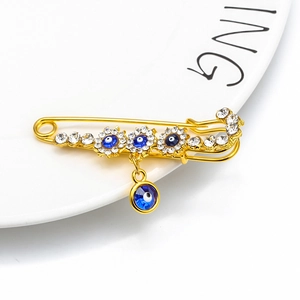 Detailed macro view of golden evil eye safety pin brooch with blue crystals on white plate