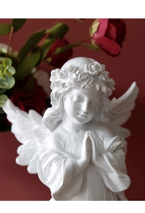 Close-up of white resin angel sculpture with flower crown praying against red background