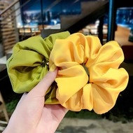 Detail view of yellow and cyan oversized satin hair scrunchies with silk-like glossy finish