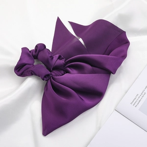 Detailed view of a purple satin bow scrunchie on silk background with an open book