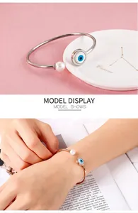 Detail show of adjustable open bangle featuring evil eye charm and white pearl