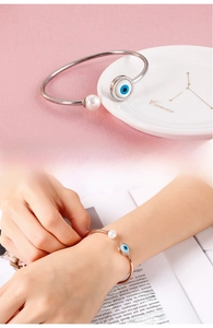 Detail show of adjustable open bangle featuring evil eye charm and white pearl