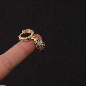 Macro view of gold hoop earring with colorful stones and teardrop pendant on finger