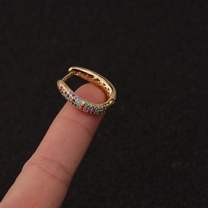 Close-up of golden U-shaped earring with colorful gemstones held on a fingertip