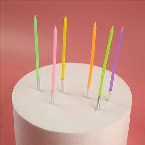 Detail view of colorful long thin birthday candles with silver bases on pink background