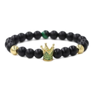 Close-up of matte black beads bracelet featuring a gold crown set with green crystals