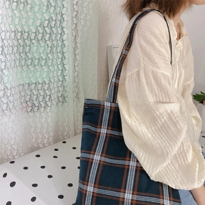Detail of dark green checkered canvas tote bag with orange grid pattern on model shoulder
