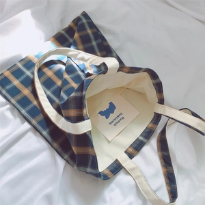 Detail of blue and tan plaid canvas tote bag with off-white handles on wrinkled fabric