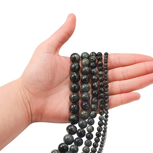 Natural green cat's eye stone round beads in multiple sizes held in hand on white background
