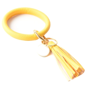 Detail of yellow leather bracelet keychain with gold metal clasp and fringe tassel charm