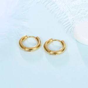 Close-up of golden stainless steel thick hoop earrings on soft blue background with feathers
