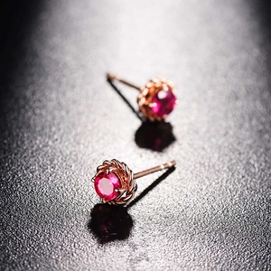 Macro detail of rose gold floral earrings featuring polished ruby gemstone centers