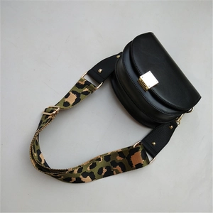 Close-up of a black leather saddle bag with green leopard print wide shoulder strap