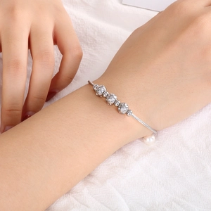Bracelet torsadé argenté avec sphères en zircon et perle sur poignet et tissu blanc