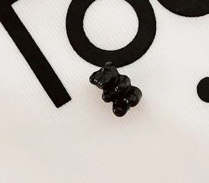 Close-up of a cute black gummy bear pin on white fabric with minimalist text detail
