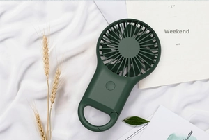 Detail of dark green portable mini fan with integrated carabiner handle on white fabric